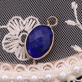 Lapis lazuli oval faceted gemstone pendant with golden frame on white lace background - 11x19mm / Lapis Lazuli