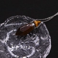 Macro view of a hexagonal tiger eye stone perfume bottle pendant with silver chain - Tiger's Eye