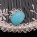 Detalle del colgante ovalado de piedra natural azul claro con anillo dorado sobre encaje - Calcedonia Azul