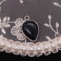 Macro shot of a teardrop black agate pendant with silver metal frame on lace background - Black Agate