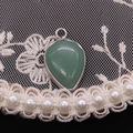 Macro shot of green teardrop stone pendant with silver metal bezel on lace background - Green Aventurine