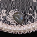 Close-up of a pear-shaped grey labradorite pendant with blue sheen and silver metal rim - Flash Stone (Labradorite)