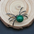 Macro shot of spider-shaped pendant with a green gemstone on a natural wood slice - 34x47mm / Green Stone (No. 11)