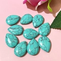 Flat lay of ten teardrop-shaped turquoise stones with black veins on a pink floral background - 17x24mm / Turquoise