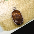 Macro shot of oval tiger eye pendant with silver plated edge and golden brown texture - Tiger's Eye