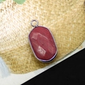 Macro detail of oval faceted red natural stone pendant with silver plated bezel setting - Rhodonite