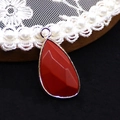 Close-up of faceted red opal teardrop pendant with silver frame on lace base - 14x27mm / Red Jasper