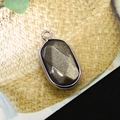 Macro shot of oval picture stone pendant with silver plated edge on textured background - Gold Obsidian