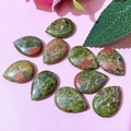 Flat lay of ten polished Unakite teardrop stones on a pink floral background - 17x24mm / Unakite