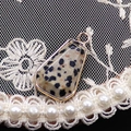Vista macro di un ciondolo in pietra naturale a trapezio con bordo dorato e perle - Diaspro dalmata