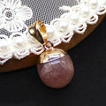 Anhänger in Eichelform aus rosa Quarz mit goldener Kappe auf weißem Spitzenhintergrund - Erdbeerquarz