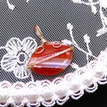 Detailed close-up of wire-wrapped oval red striped agate pendant on white lace - 14x21mm (3g) / Red Striped Agate (No. 1)