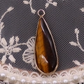 Détail d'un pendentif en œil de tigre en forme de goutte avec bordure dorée sur dentelle - Œil de tigre