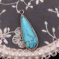 Gros plan détaillé d'un pendentif goutte d'eau en pierre bleu clair facettée et doré - Turquoise Bleue