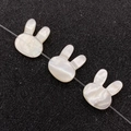 Three rabbit-shaped white mother of pearl shell beads with iridescent glow on black texture - Rabbit Head Shape / 10x12mm / White Shell (Horizontal Hole)