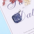 Macro shot of rhombus natural blue stone pendant with silver bail on art card - Blue Spot Stone