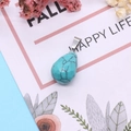 Detailed macro view of a faceted teardrop turquoise pendant with elegant floral decoration - 13x23mm / Blue Turquoise