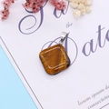 Tiger Eye stone pendant in square shape with silver bail on a light blue background - Tiger's Eye