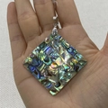 Pendentif losange en mosaïque de nacre d'abalone aux reflets irisés tenu à la main - Style Losange
