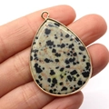 Dalmatian Jasper teardrop pendant with gold-plated edges held between fingers - Dalmatian Jasper