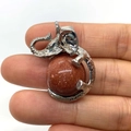 Elephant-shaped silver alloy pendant with brown goldstone ball held in hand - 21x32mm / Gold Sandstone