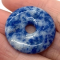 Polished blue and white sodalite donut pendant on palm showing natural mineral textures - Blue Spot Stone