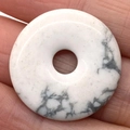 Natural white marble textured stone donut pendant held between fingers showing polished finish - Howlite