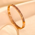 Macro shot of gold stainless steel bangle with Greek key engraving on apricot satin fabric - 18K Gold / Rose Gold Hollow Greek Key
