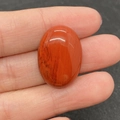 Gepolijste rode jaspis ovale cabochon met natuurlijke texturen getoond op vinger - Red Jasper (No. 24) / 18x25mm