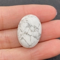 Gepolijste witte howliet steen in ovale vorm met grijs marmerpatroon in de hand - Howliet / 18x25mm