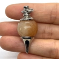 Natural warm orange stone ball pendant in silver metal setting held by hand - Yellow Agate (No. 16)
