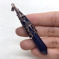 Detailopname van een zeshoekige blauwe goudsteen hanger met koperen zetting in de hand gehouden - Blauwe zandsteen