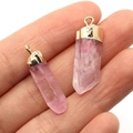 Hand met twee roze kwarts hangers in kolomvorm met gouden metalen kapjes erop - Zeshoekige Kolom Rozenkwarts (Nr.2) / Roze
