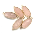 Detailed close-up of faceted pink crystal oval pendants with gold plated metal frames - Rose Quartz