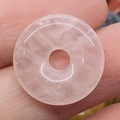 Donut-Anhänger aus rosa Quarz mit weißem Linienmuster zwischen den Fingern - Rosenquarz