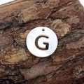 Macro detail of natural freshwater shell pendant with hollow letter G on bark surface - Letter G