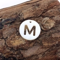 Natural white shell pendant featuring a cutout letter M design on rustic bark - M