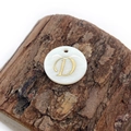 Detailed view of a shell pendant with a golden letter D on a rustic wood background - Letter D