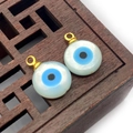 Vue macro de pendentifs en nacre œil grec avec bélière dorée sur fond en bois foncé - Rond 4mm