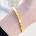 Golden titanium steel bangle with engraved vintage meander pattern on female wrist - Gold