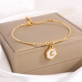 Elegante pulsera de acero de titanio dorado con dije de luna sobre fondo de seda - Luna de Esmalte Dorado
