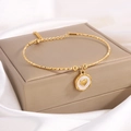 Primer plano del brazalete dorado con colgante de corazón sobre caja de exhibición de joyas - Corazón de Esmalte Dorado