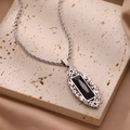 Vue macro d'un pendentif en obsidienne noire avec filigrane argenté sur fond de soie - Style Rectangulaire Creux / Collier Filigrane Argent Zirconium Noir