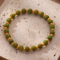 Vue détaillée des perles de céramique vertes et billes dorées sur plateau en pierre - Bracelet À Perles Vertes