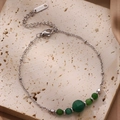 Vue macro d'un bracelet en acier inoxydable argenté avec cinq perles vertes - Vert