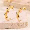 Vue macro de boucles d'oreilles dorées en C avec pierres colorées sur base en pierre - Design de Feuille