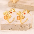 Gros plan de boucles d'oreilles vintage en or avec gemmes rouges et fleurs sur pierre - Style Trèfle