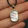 Macro detail of a gold-edged rectangular shell pendant on a black cord held in hand - Black Mother of Pearl Necklace