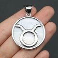 Macro shot of silver circular Taurus zodiac pendant with white mother of pearl inlay - 32x37mm / Taurus
