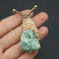 Detailed close-up of a gold snail brooch featuring a natural green spiral conch shell - Green Snail Brooch / 20-60mm, 11-17g / Gold